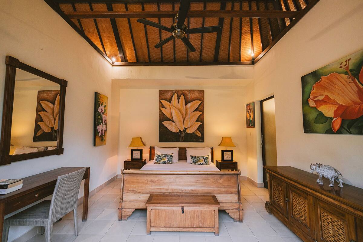A bedroom with a wooden bed, bedside tables with lamps, a desk, and a bench.