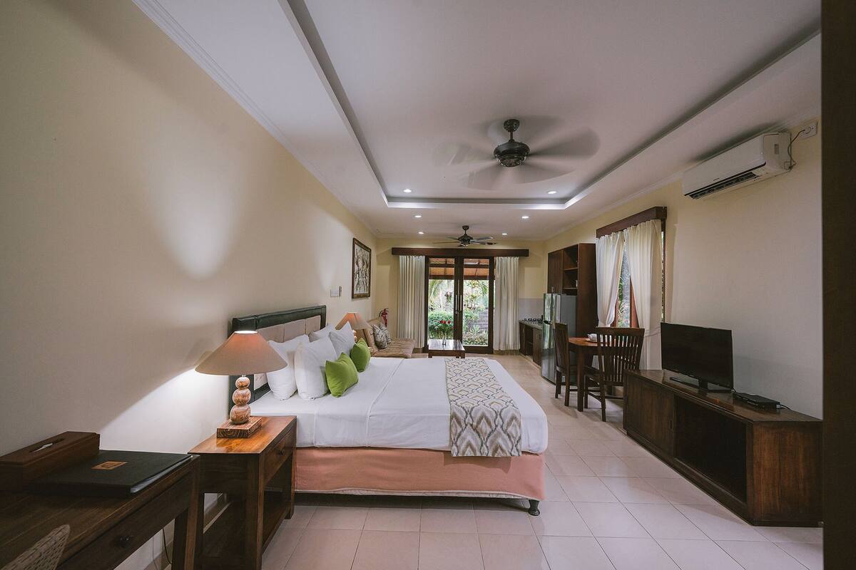 A hotel room with a bed, bedside table, lamp, TV, and a desk with a chair.
