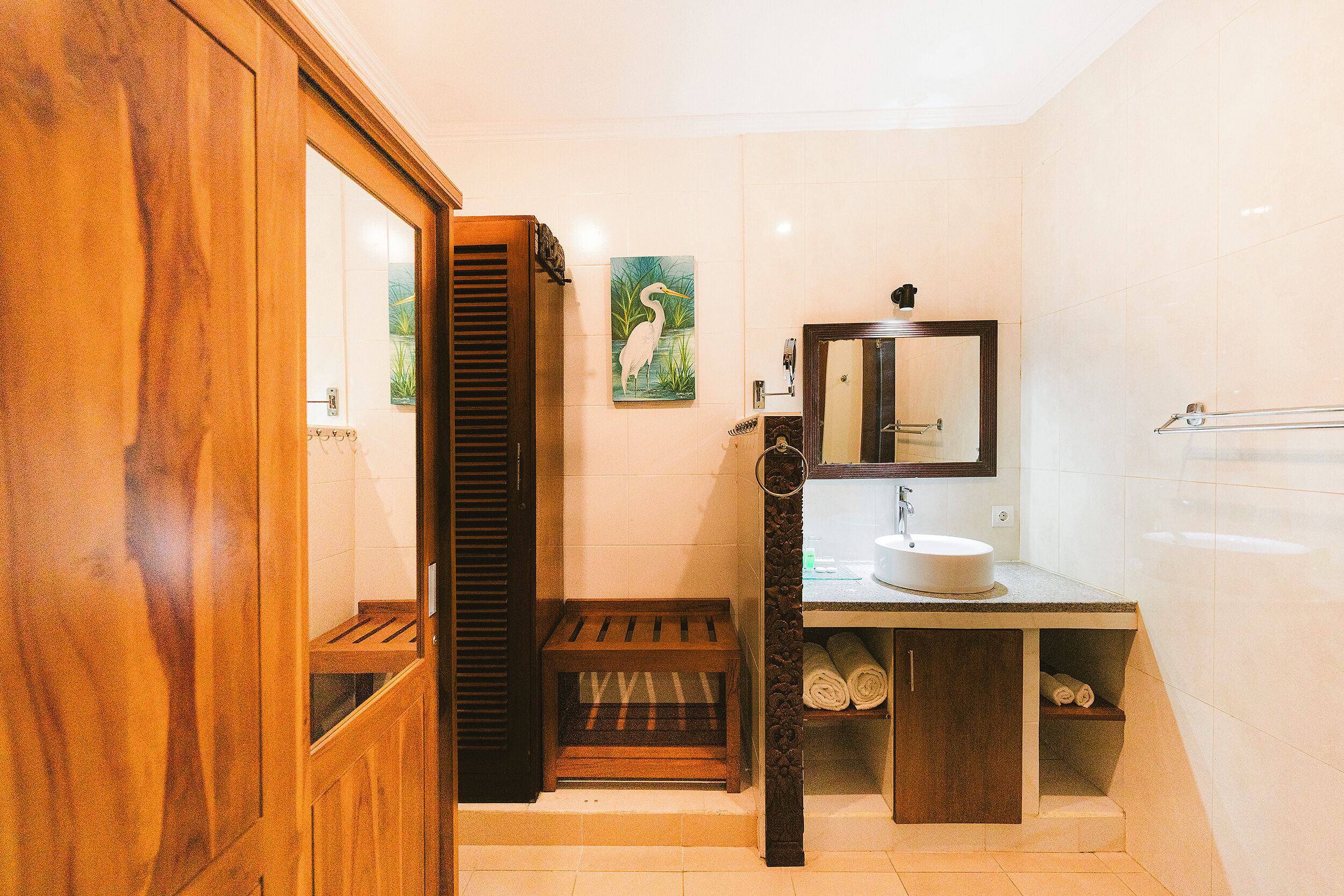 Un baño con banco de madera, lavamanos, espejo y toallero.