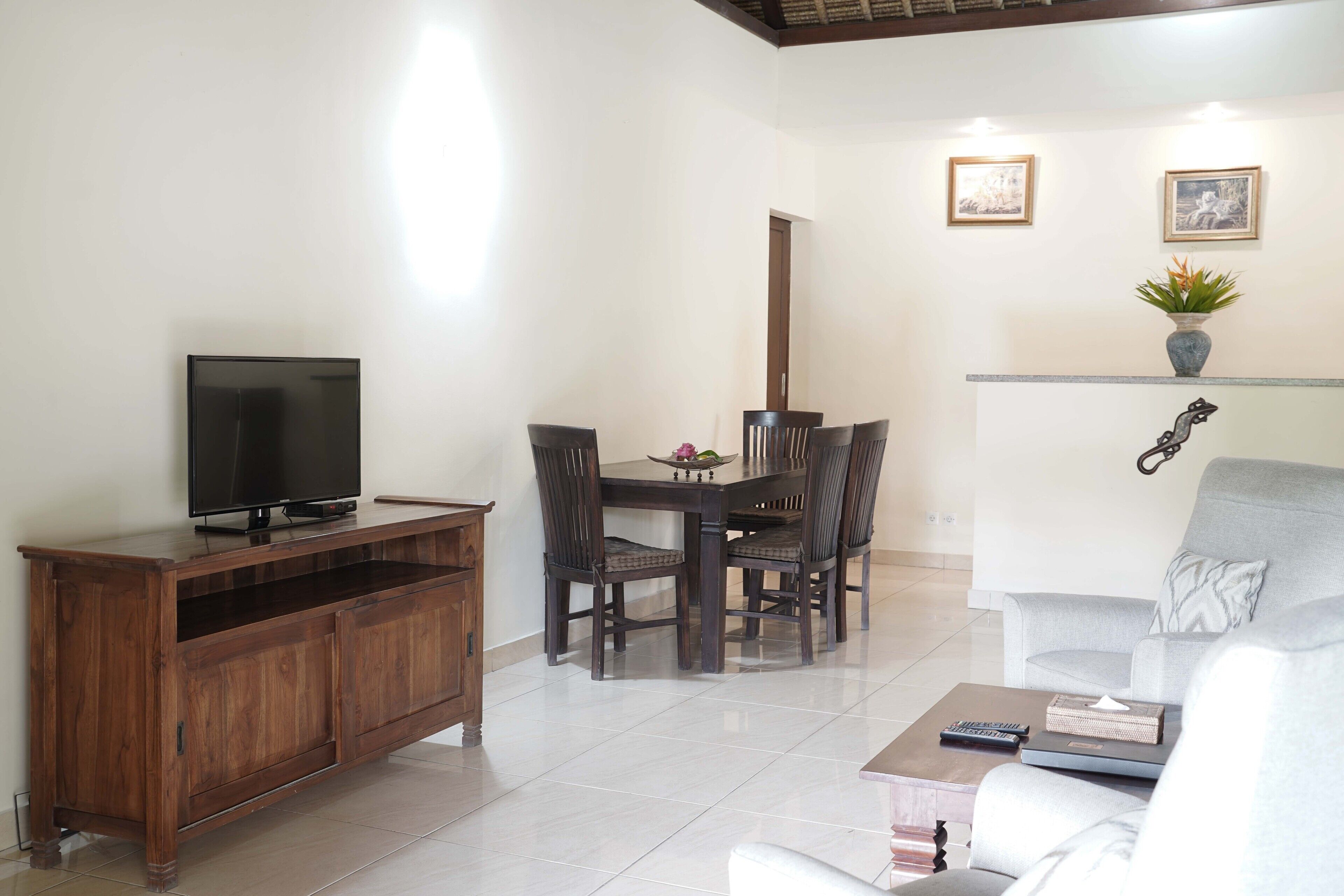 Uma sala de estar com televisão sobre um armário de madeira, uma mesa de jantar com cadeiras, um sofá e uma mesa de centro.