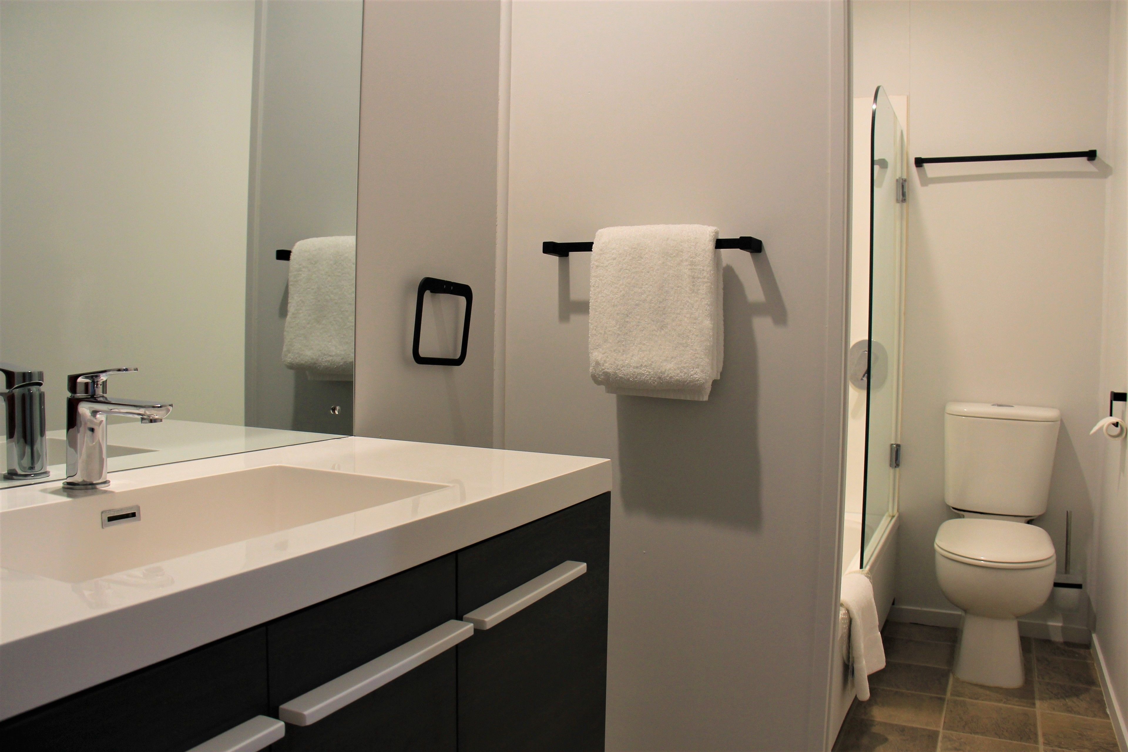 Een moderne badkamer met een wit wastafelmeubel, een spiegel, een handdoekhouder en een toilet.