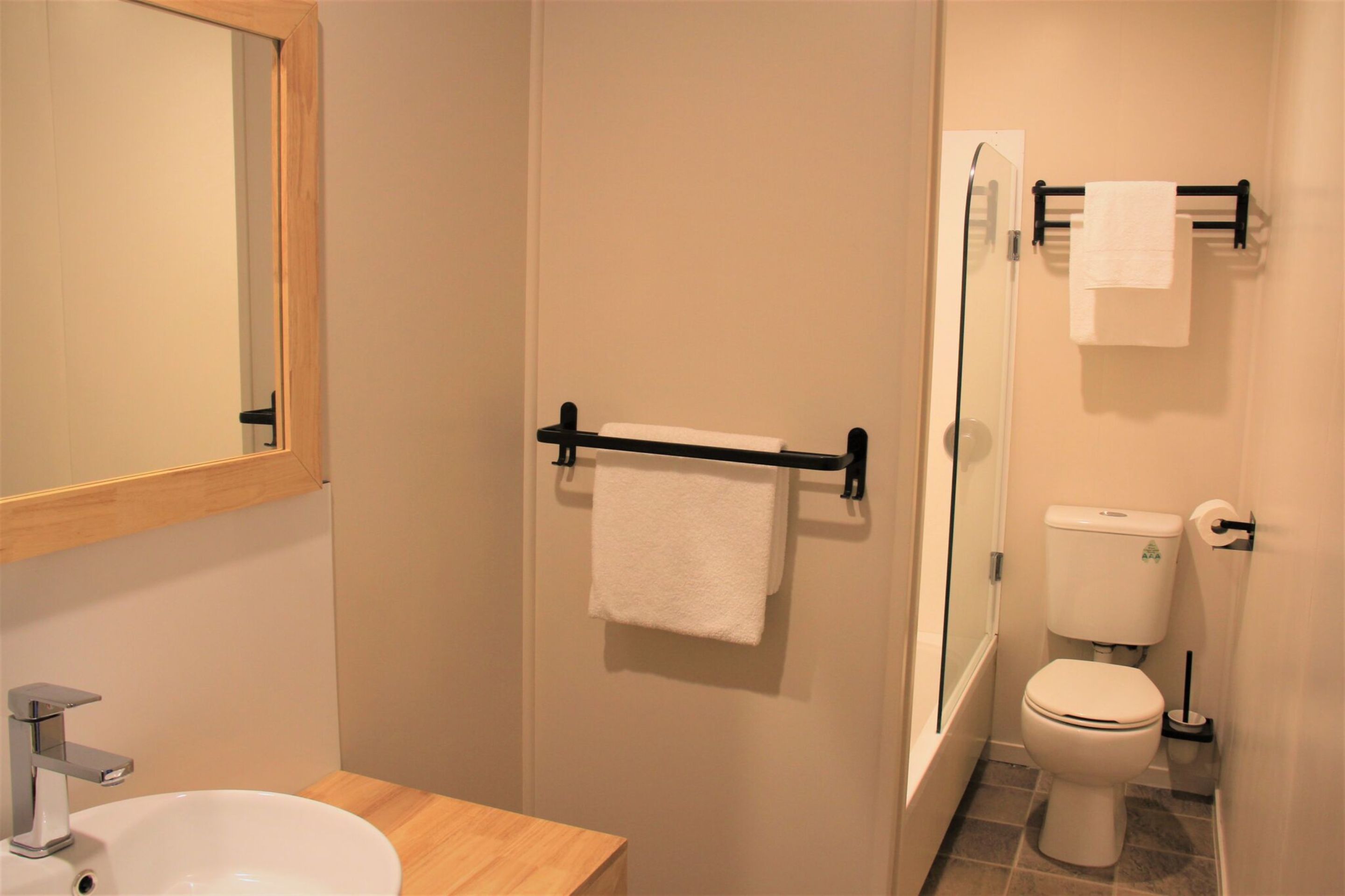 A bathroom with a sink, mirror, towel rack, toilet, and shower.