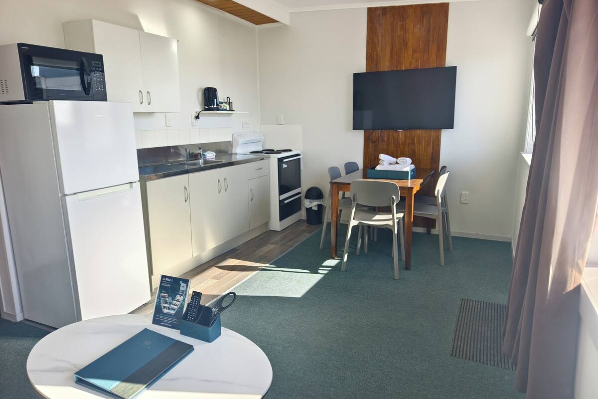A modern kitchen with white cabinets, a microwave, a coffee machine, and a dining area with a table and chairs.