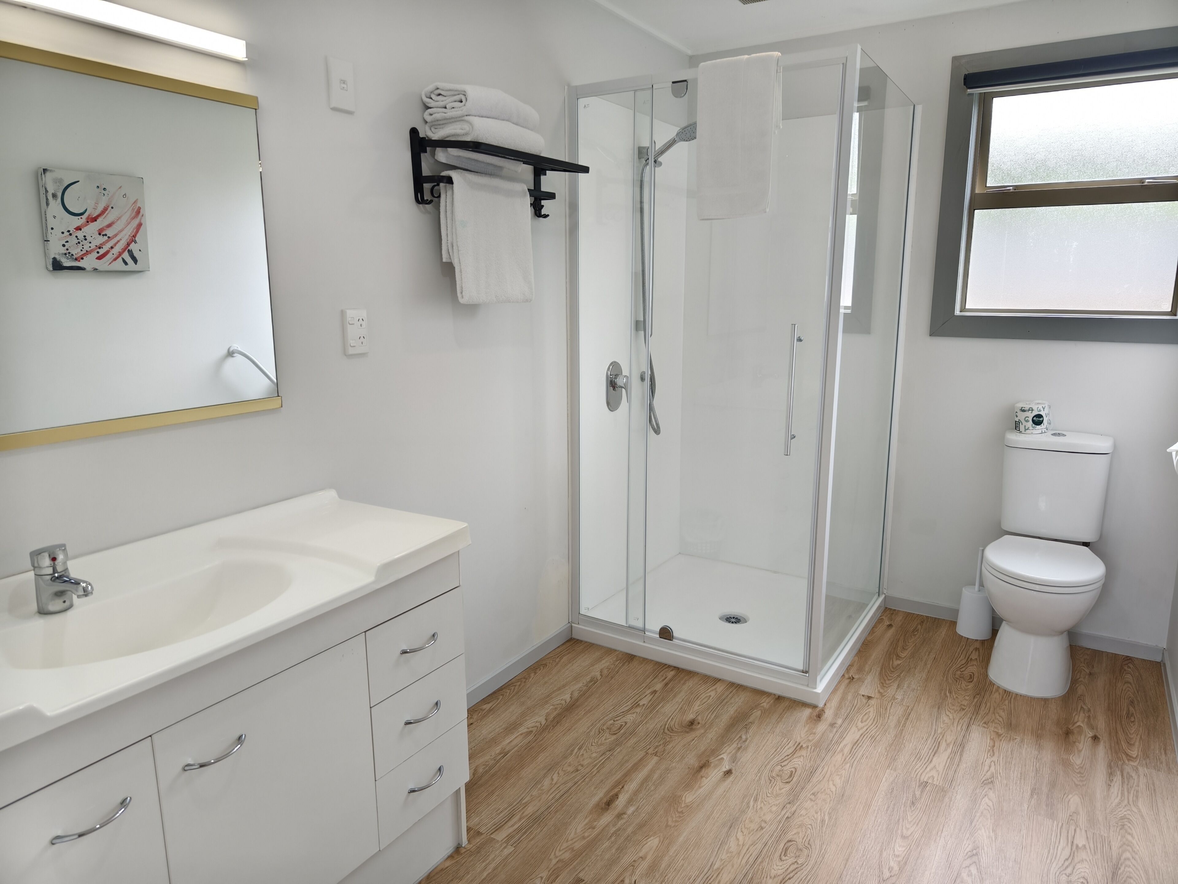A modern bathroom with a glass-enclosed shower, white fixtures, and a wooden floor.