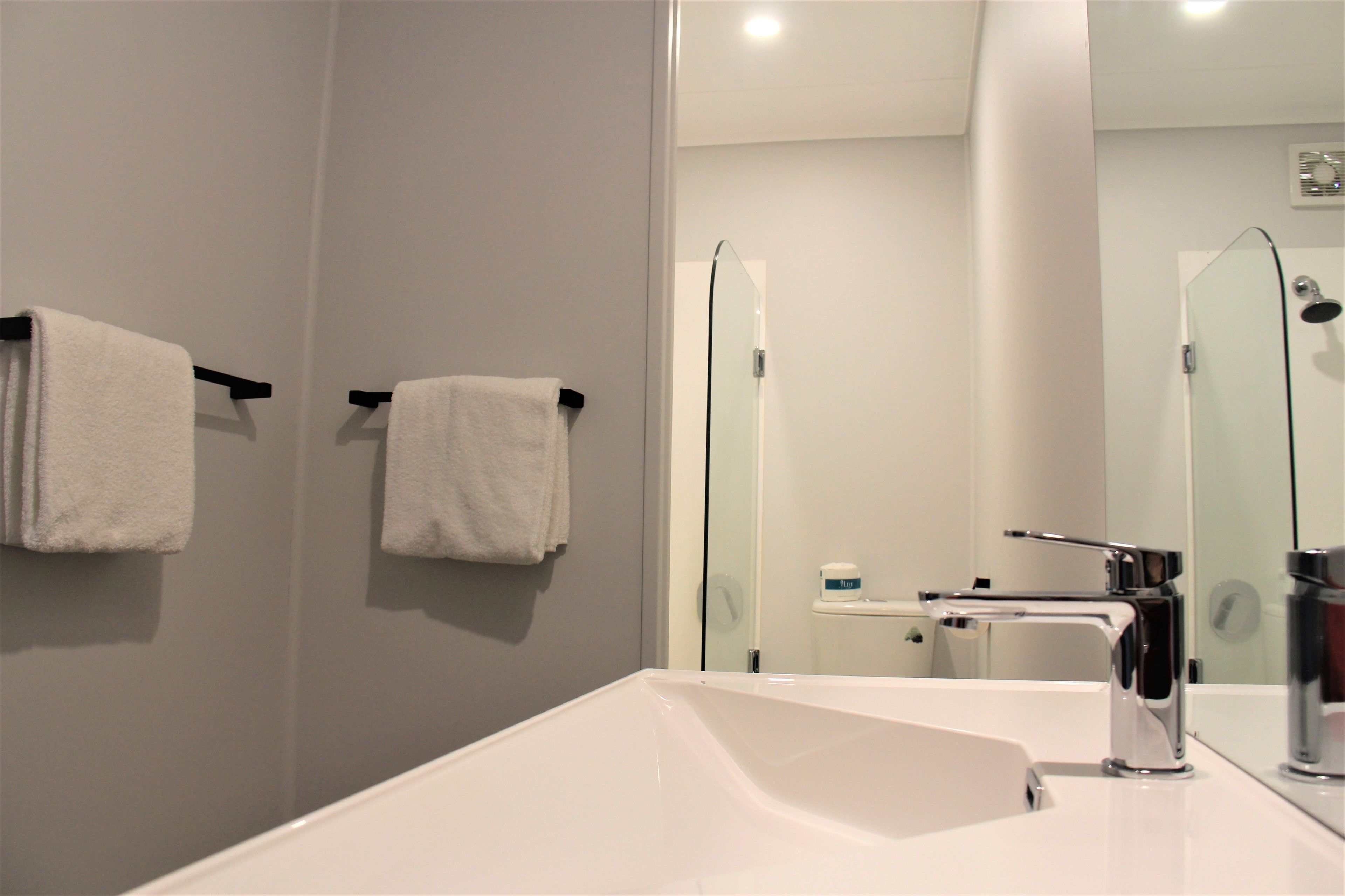 A modern bathroom with a white sink, chrome faucet, and a glass shower enclosure.