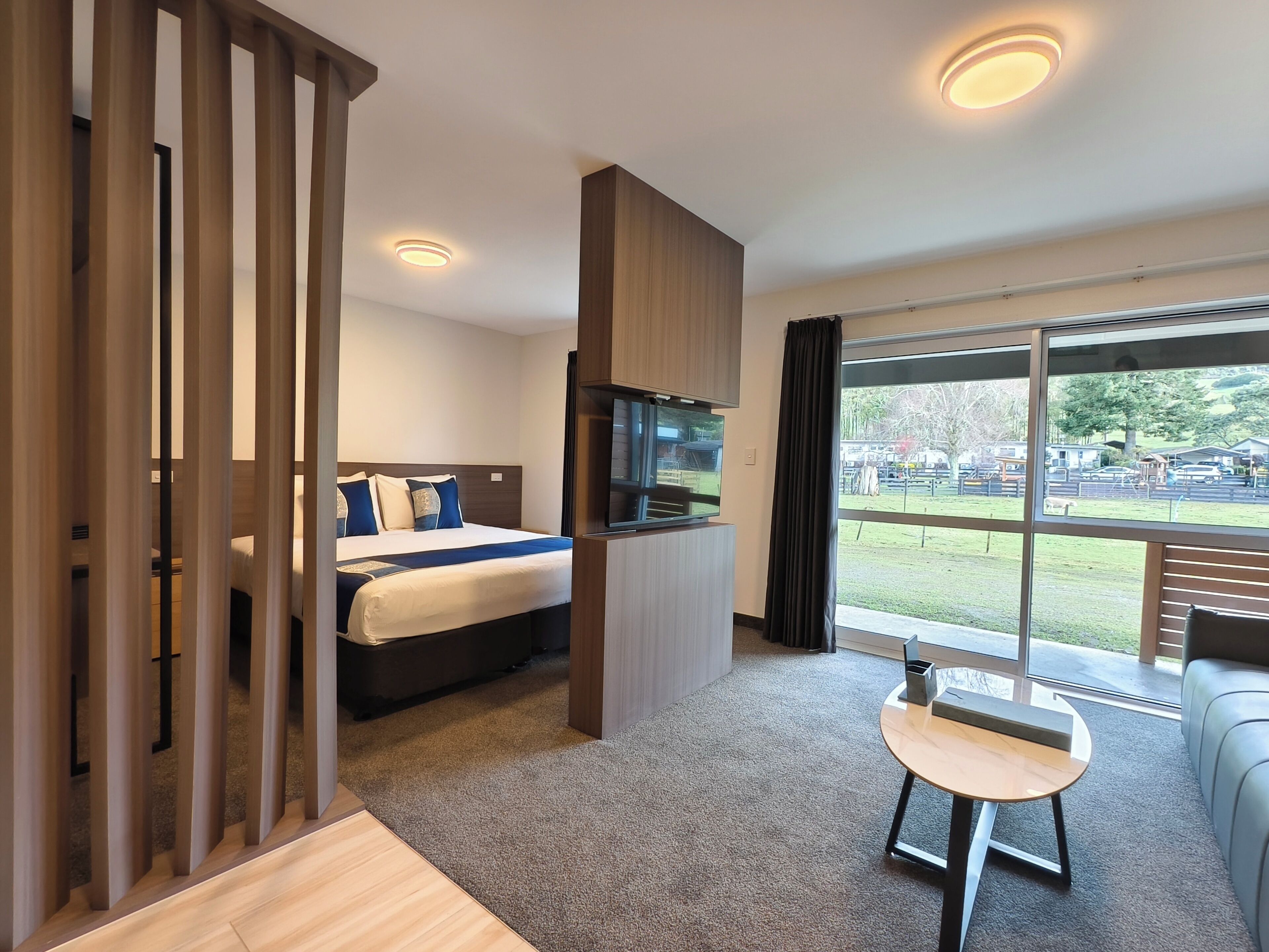 A hotel room with a bed, a TV, a small table, and a view of the outside.