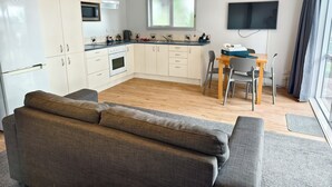 Una cocina moderna con armarios blancos, un microondas y una estufa. Hay un comedor con una mesa y sillas, y un televisor montado en la pared.