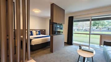 Una habitación de hotel moderna con una cama, un televisor, una mesita y un ventanal grande con vistas al exterior.