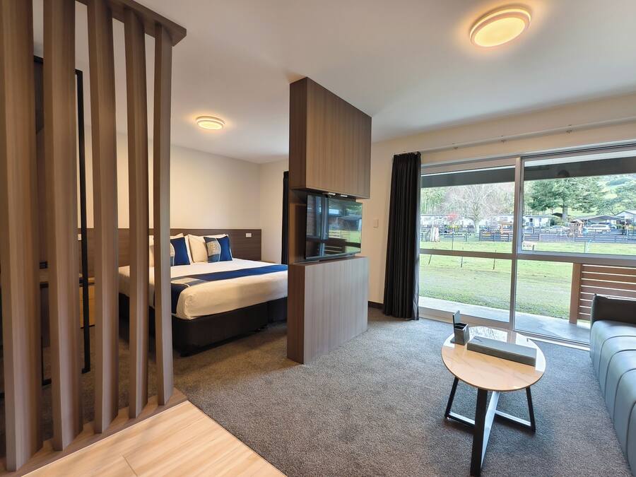 Una habitación de hotel moderna con una cama, un televisor, una mesita y un ventanal grande con vistas al exterior.