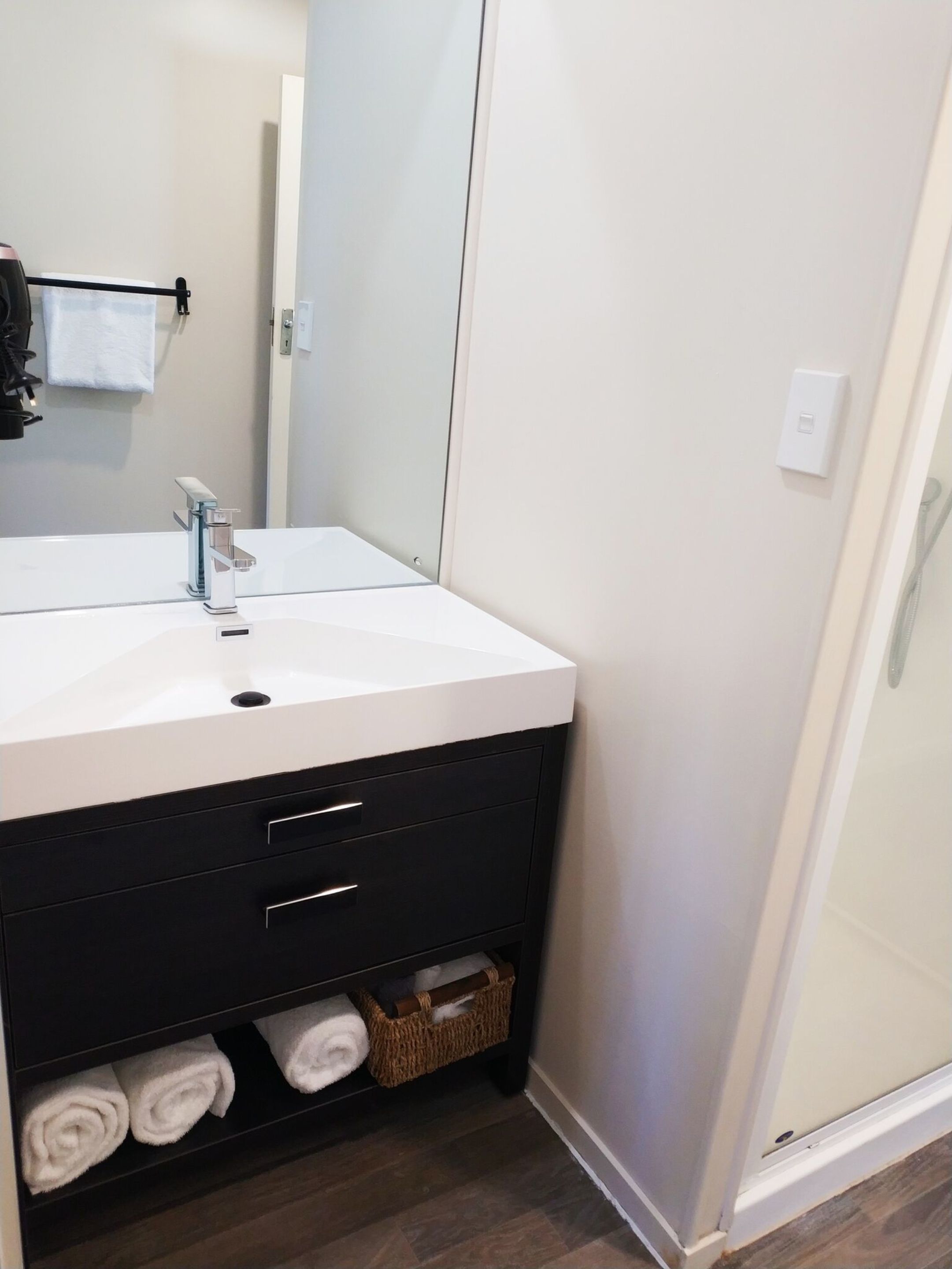 A bathroom with a white sink, black vanity, and a glass shower enclosure.
