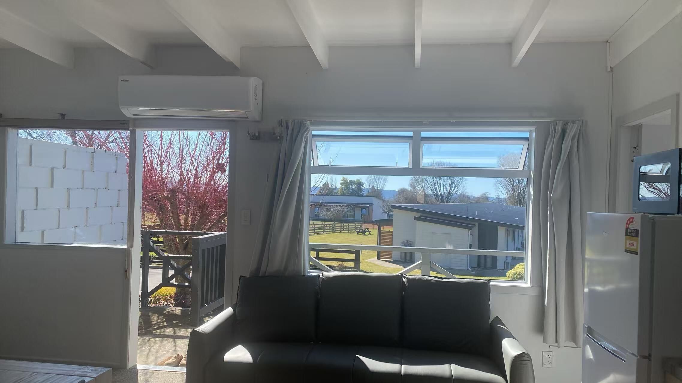 Una habitación con sofá, ventana con cortinas, refrigerador y aire acondicionado.