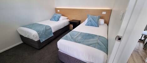 A hotel room with two beds, each with a headboard, bedside tables, and a carpeted floor.