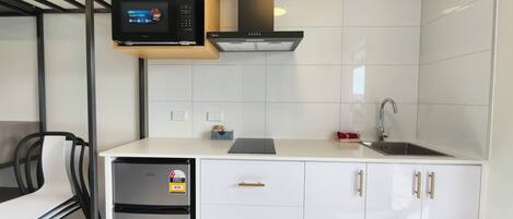 A compact kitchen with white cabinetry, a built-in microwave, a stainless steel dishwasher, and a gas stove.
