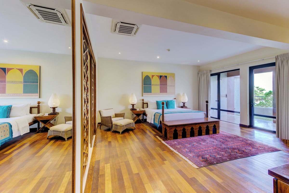 Quarto espaçoso com uma cama grande, duas mesas de cabeceira com luminárias, um banco de madeira, um tapete estampado e uma janela ampla com vista para o exterior.