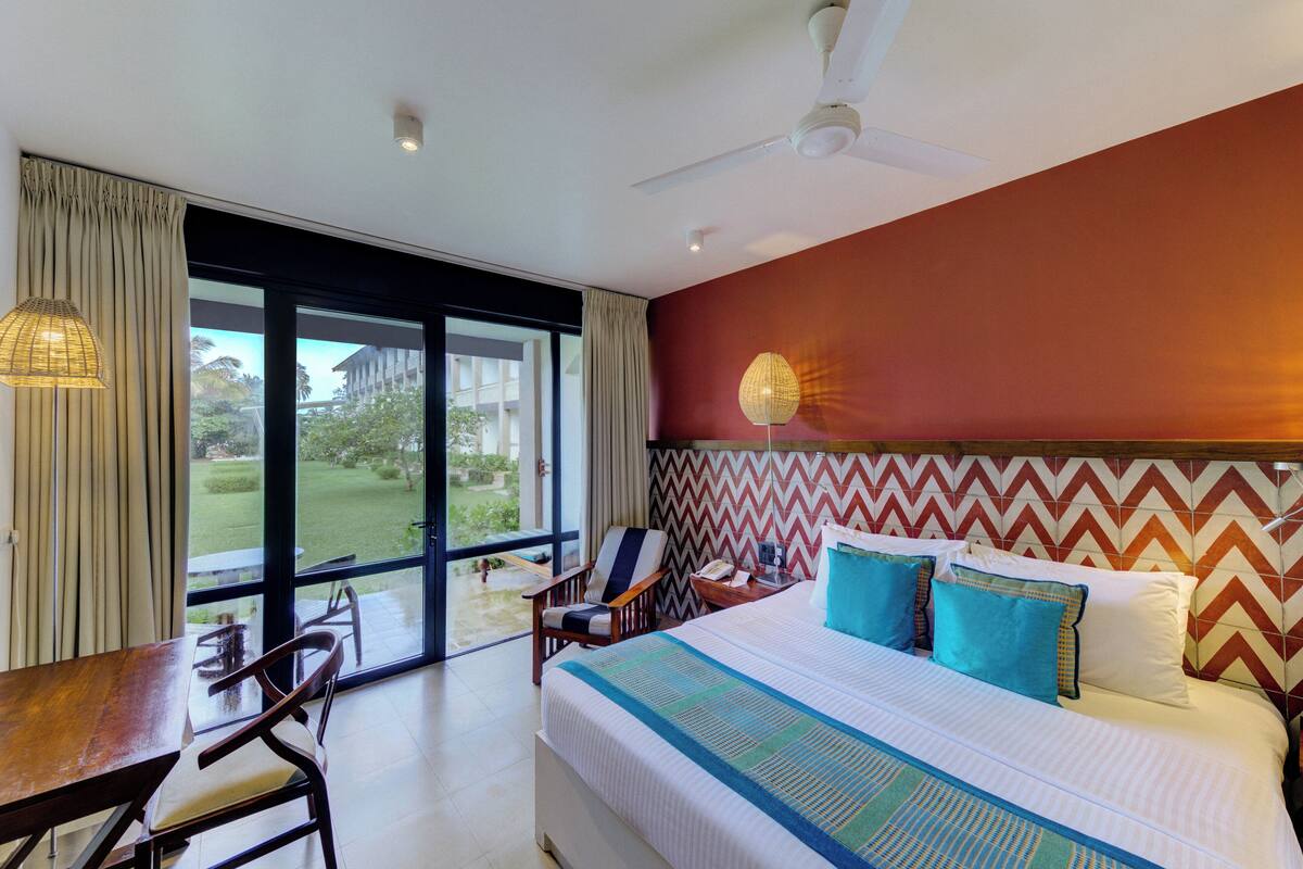 Quarto de hotel com uma cama, uma escrivaninha e uma cadeira. Há vista do exterior através de grandes janelas.