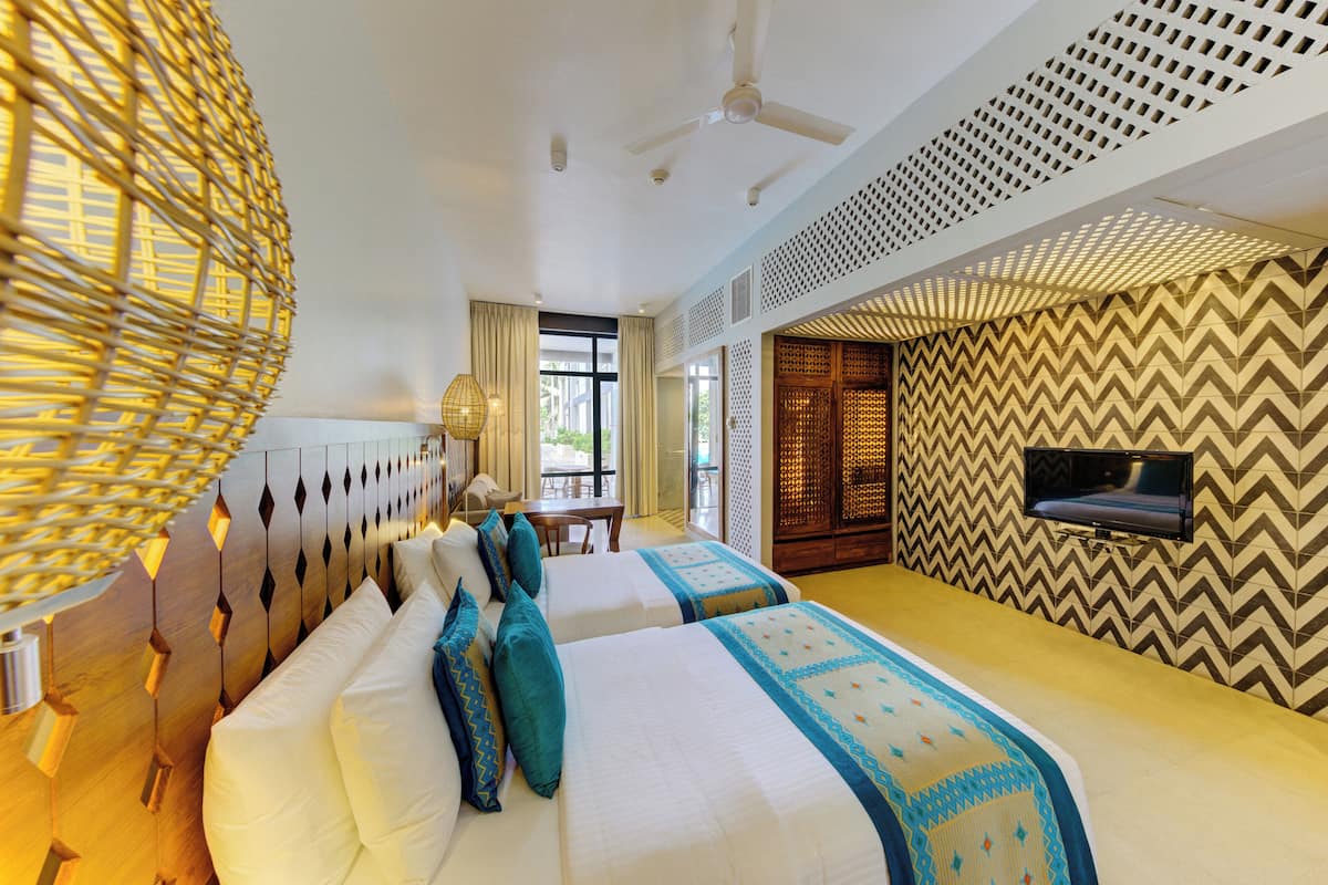 Quarto de hotel com duas camas, um ventilador de teto, uma televisão e um papel de parede estampado.