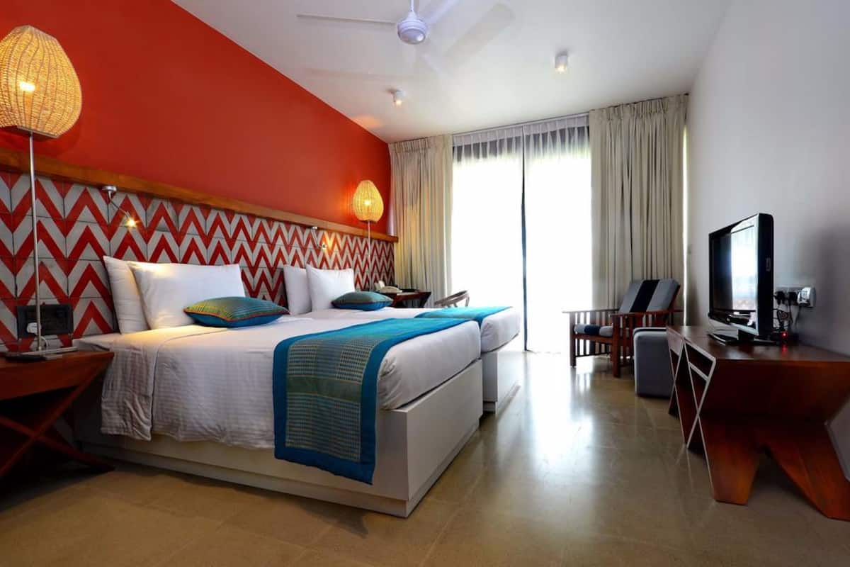 Quarto de hotel com cama, escrivaninha, televisão e ventoinha no teto.