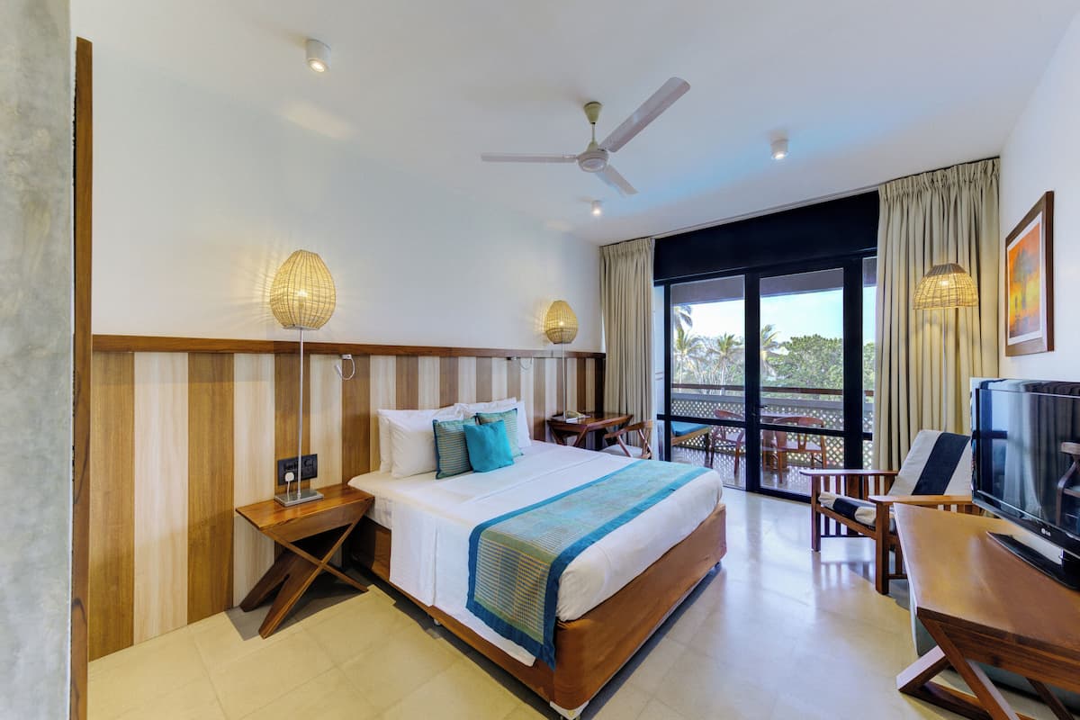 Quarto de hotel com uma cama grande, uma escrivaninha, uma televisão e uma varanda com vista.