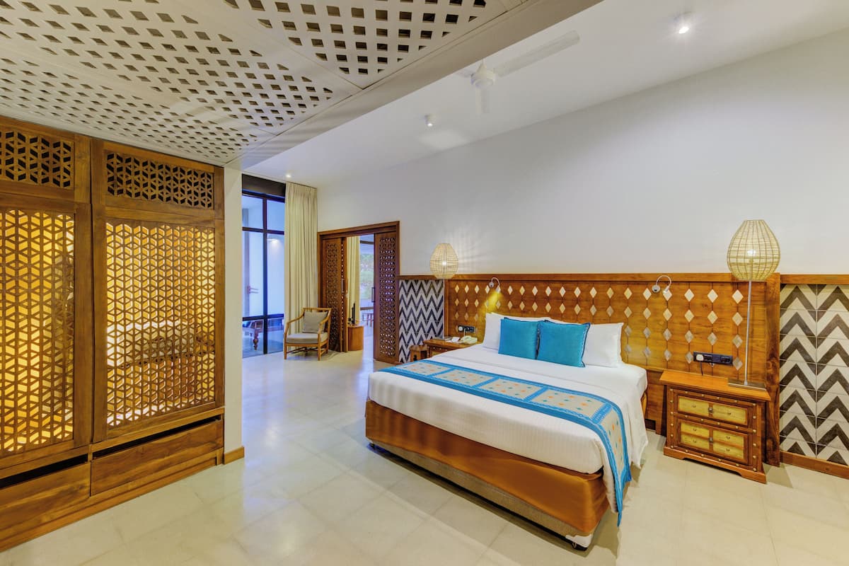 Quarto de hotel com cama grande, cabeceira de madeira e divisória decorativa.