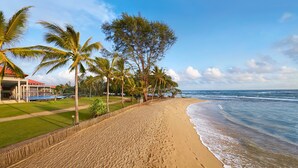 A beach with palm trees, a wooden fence, and a building with a red roof. - Cinnamon Bey Beruwala (Beruwala)