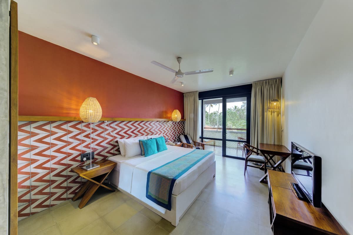 Quarto de hotel com cama, escrivaninha, cadeira, televisão e ventoinha no teto.