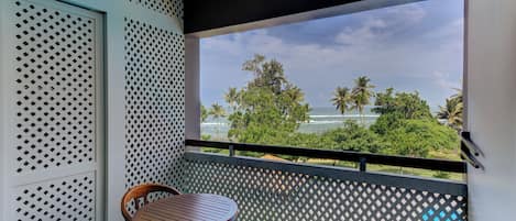 A balcony with a view of palm trees and the sea, a wooden chair, and a table.