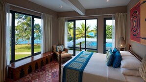 A hotel room with a large bed, a bench, and a view of a pool and palm trees. - Cinnamon Bey Beruwala (Beruwala)