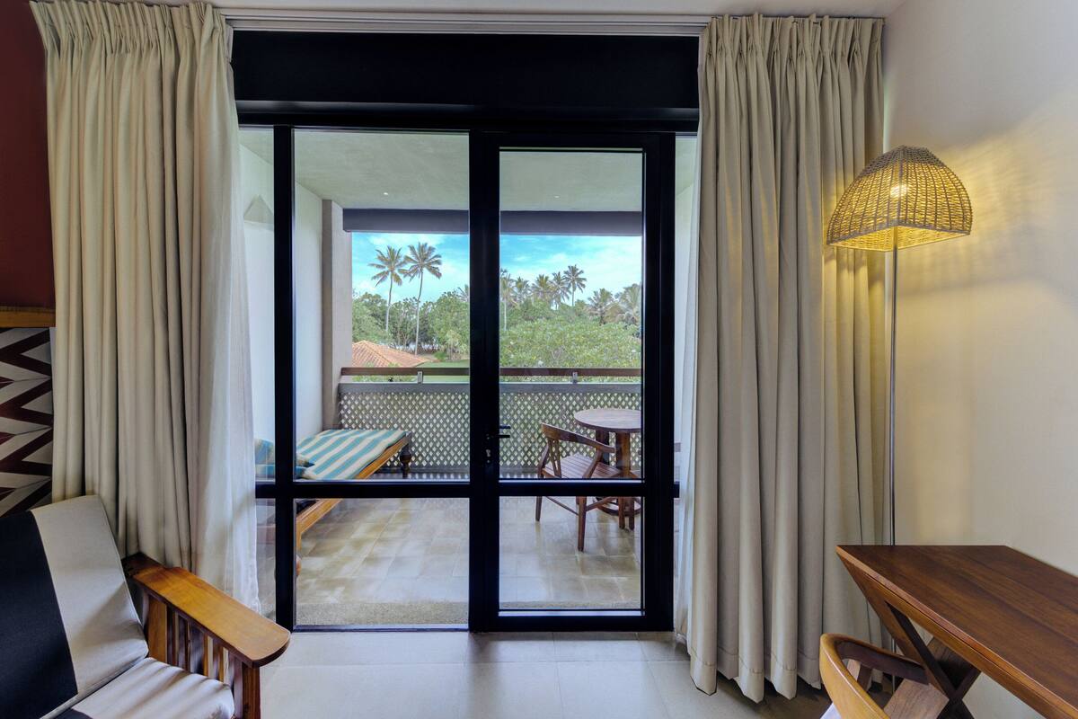 Quarto com porta de vidro deslizante que dá para uma varanda com mesa, cadeiras, sofá e luminária.
