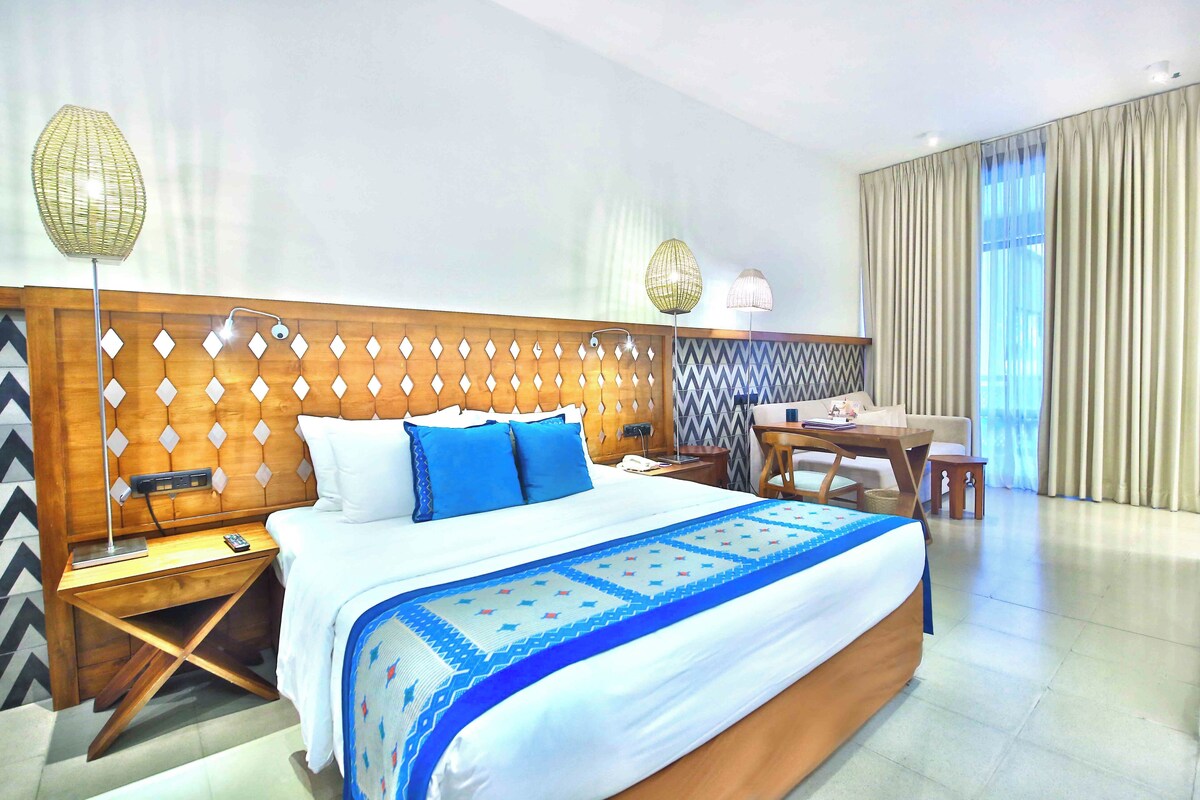 A hotel room with a large bed, wooden headboard, bedside tables, a desk, and a chair.