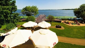 A lakeside patio with outdoor seating and umbrellas, a playground, and a view of the lake.