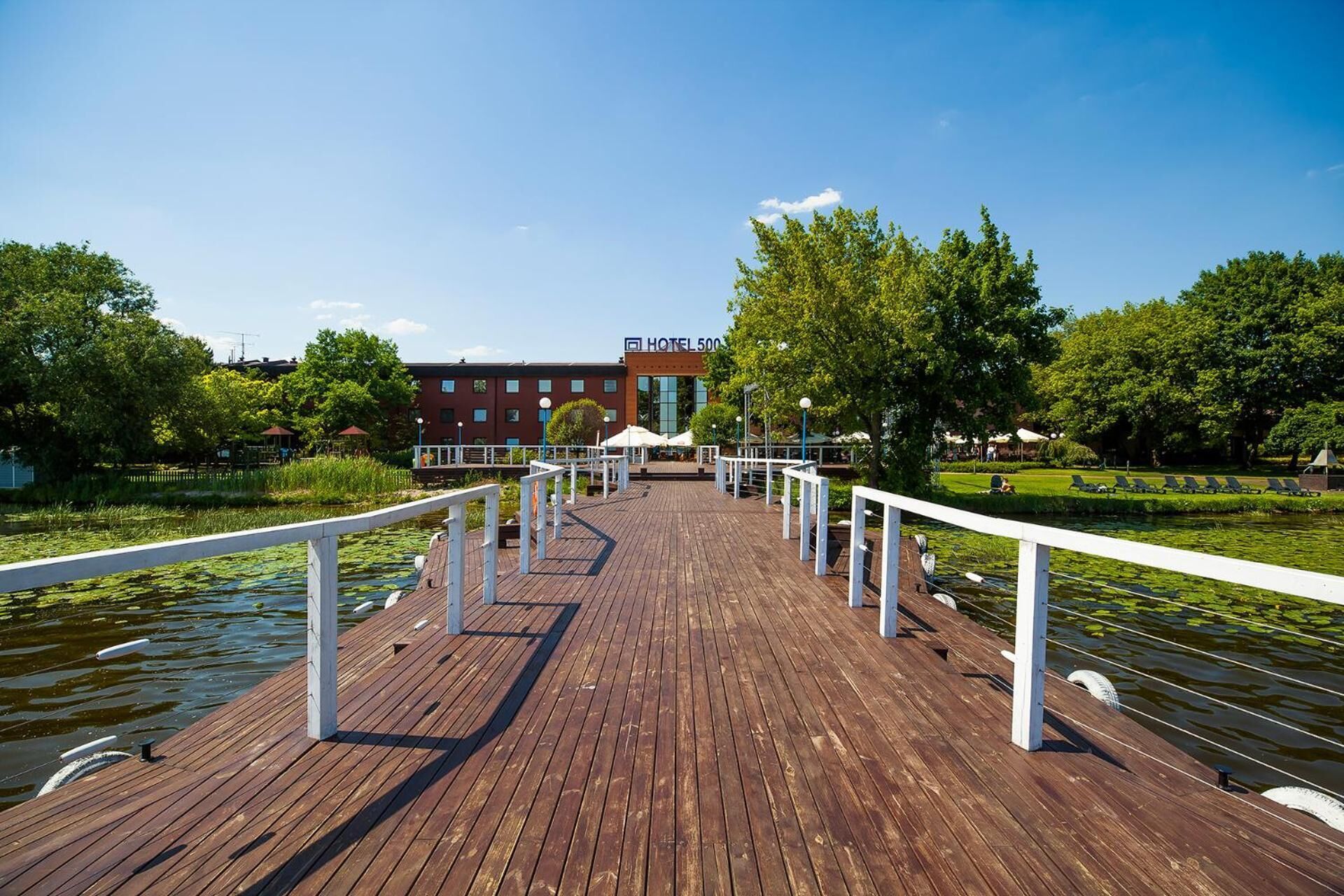 A wooden boardwalk leading to a hotel with a view of a lake and greenery.
