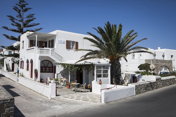 A white building with a balcony, a palm tree, and outdoor seating.