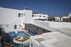 A pool area with a table set for two, lounge chairs, and a stone wall.