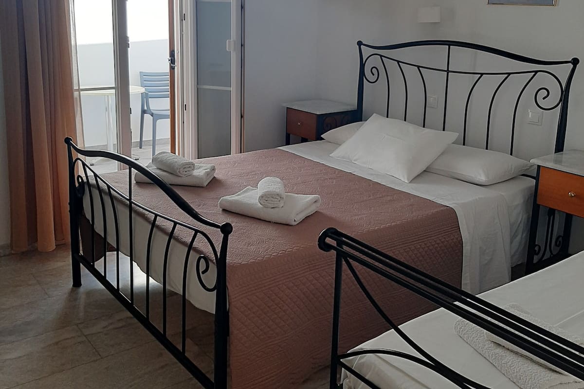 Une chambre à coucher avec un lit, une table de chevet, une chaise, une fenêtre avec des rideaux et un tableau au mur.