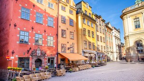 A cobblestone street with outdoor seating at a café, surrounded by colorful buildings with classical architecture.