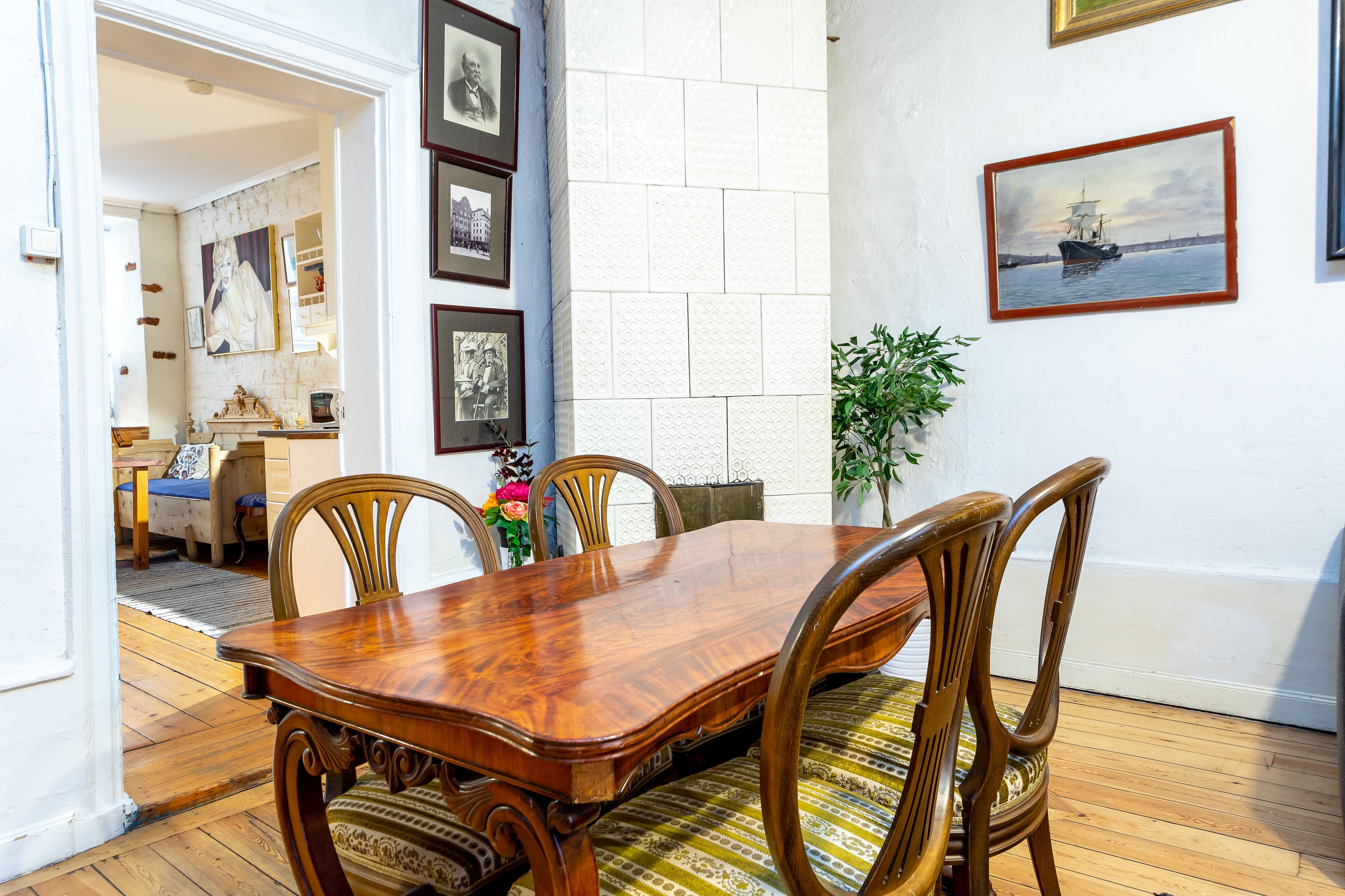 Un comedor con una mesa y sillas de madera, un muro de azulejos blancos y cuadros enmarcados.
