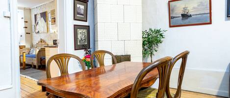 Un comedor con una mesa y sillas de madera, un muro de azulejos blancos y cuadros enmarcados.