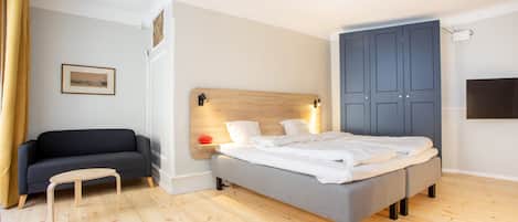 A bedroom with a bed, a sofa, a wooden floor, a wall-mounted TV, and a door.