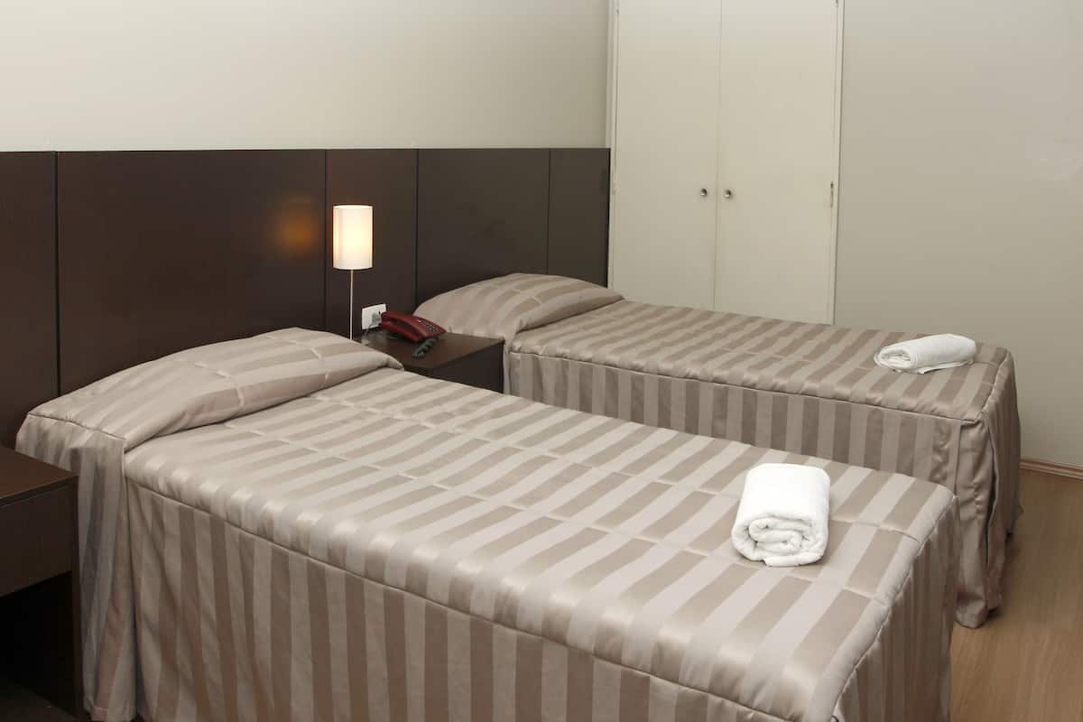 A hotel room with two single beds, a bedside table with a lamp, a telephone, and a wardrobe.
