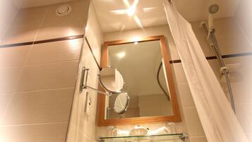 A bathroom with a glass shelf, a mirror, a shower, and a sink.