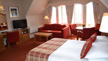A hotel room with a bed, a desk with a television, a sofa, and a dining area with a table and chairs.
