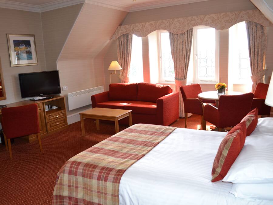 A hotel room with a bed, a desk with a television, a sofa, and a dining area with a table and chairs.