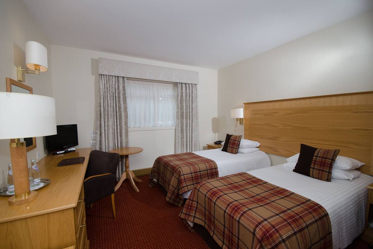A hotel room with two beds, a desk with a computer, a chair, and a television.