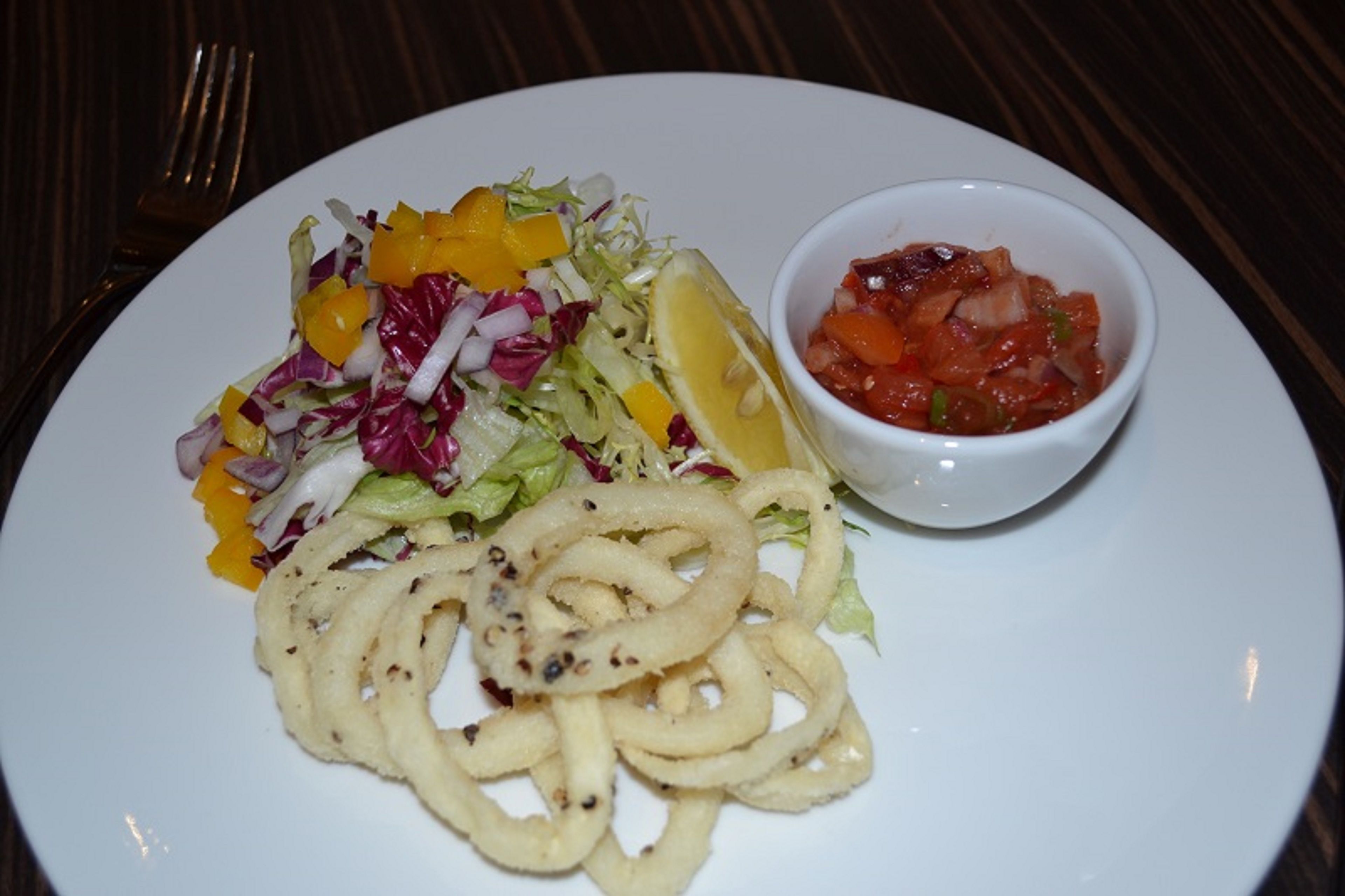 A plate with a salad, a lemon wedge, and a bowl of salsa.
