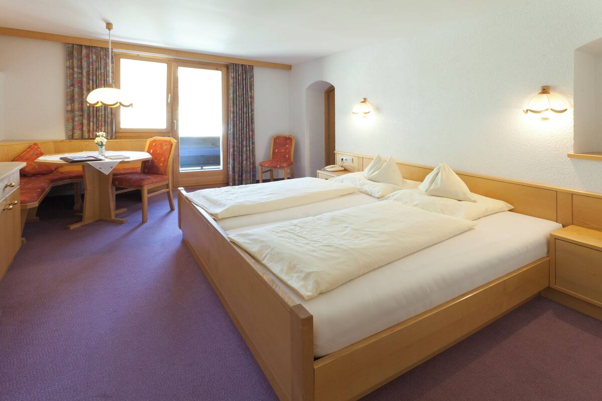 Ein Hotelzimmer mit einem Doppelbett, einem Schreibtisch mit Stuhl, einem kleinen Tisch und einem Fenster mit Vorhängen.
