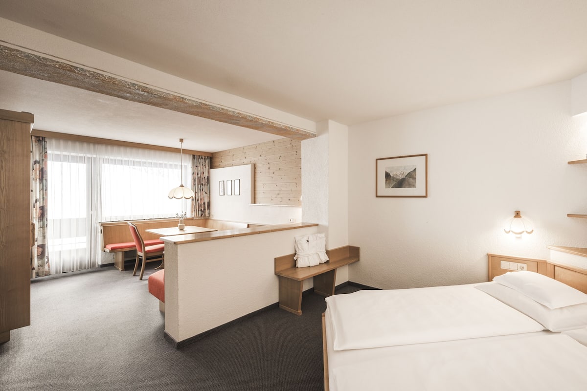 Ein Hotelzimmer mit Bett, Schreibtisch, Stuhl, kleinem Tisch, Spiegel und einem Bild an der Wand.