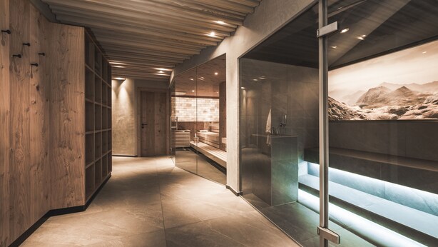 Een modern interieur met een houten wand, een douchecabine van glas en uitzicht op een bergachtig landschap.