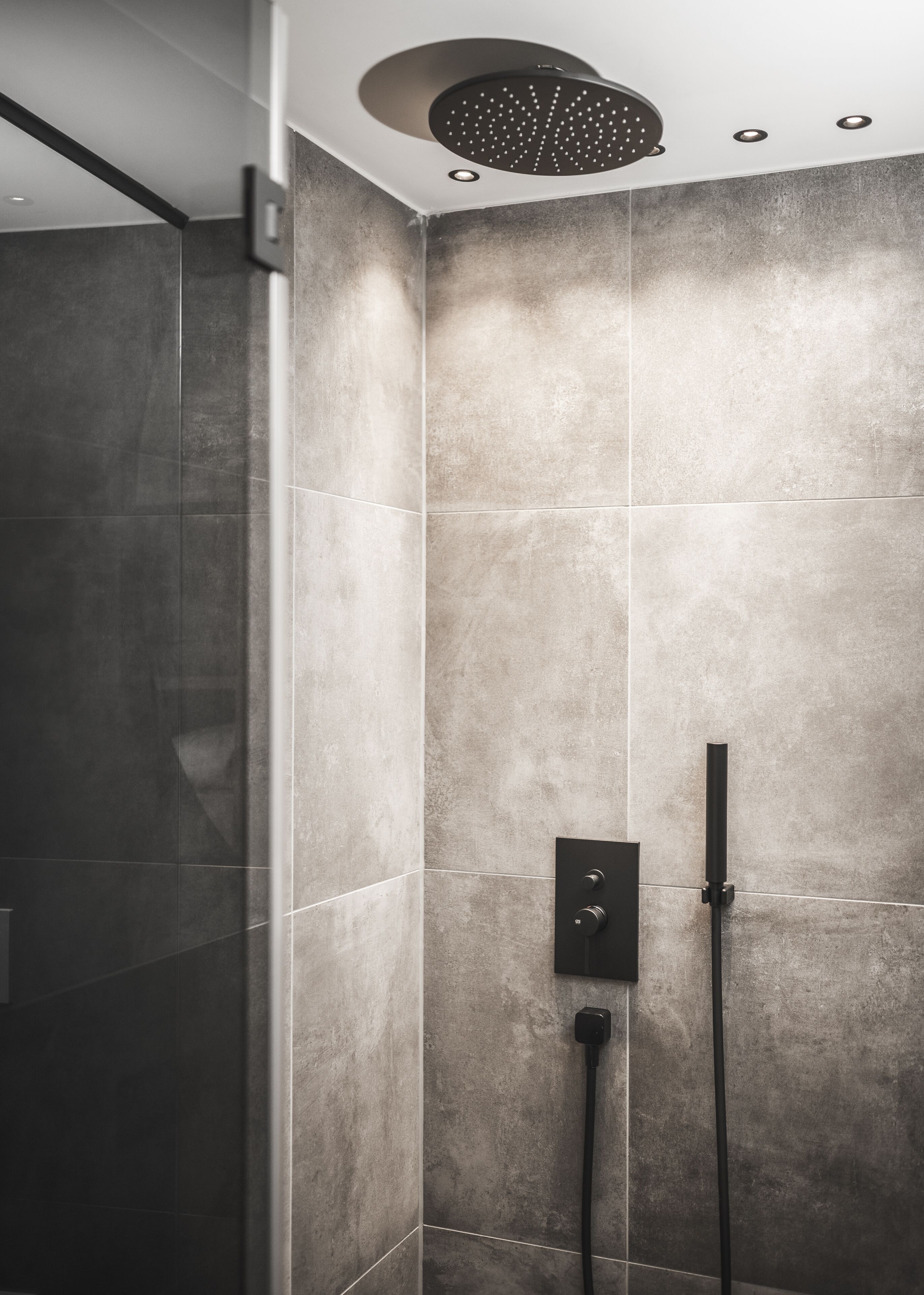 Eine moderne Duschkabine mit Regendusche und Handbrause, vor einer Wand mit strukturierter Oberfläche.