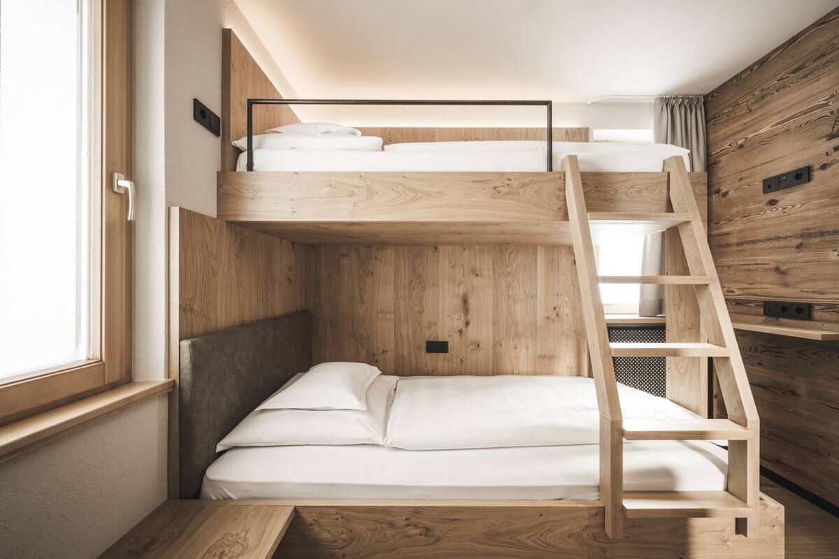 Ein Stockbett mit einer Holzleiter, einem Fenster und einer Holzwand.
