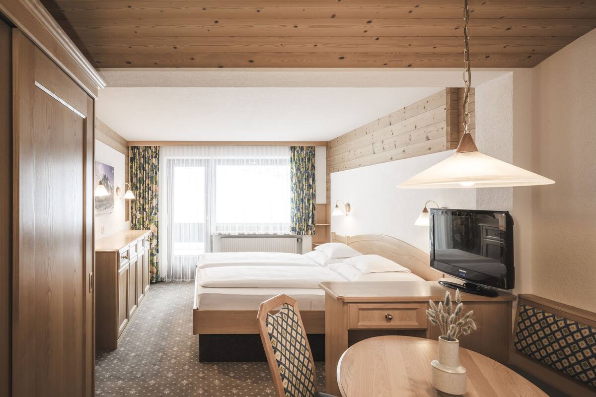 Ein Hotelzimmer mit Bett, Schreibtisch, Stuhl, Fernseher und einem Fenster mit Vorhängen.